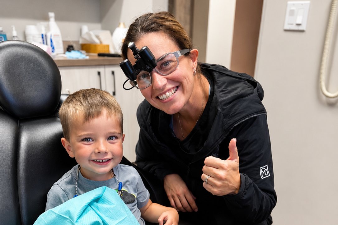 Dr. Erin Ellis giving a thumbs up beside a smiling young patient in the dental chair